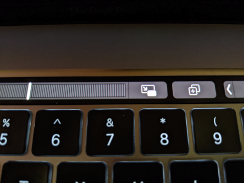 A close-up photograph of the MacBook Pro touchbar when a video is playing. There is an icon next to the playhead scrubber that opens the video in an always-on-top player window.