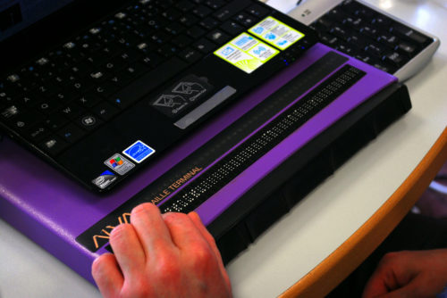 hand on purple braille terminal with laptop on top